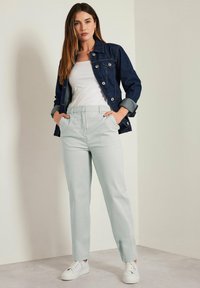 Giacca di jeans con bottoni argentati, canottiera bianca, pantaloni menta chiara e sneakers bianche. La giacca ha le maniche arrotolate e tasche classiche.