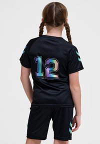 Tenue de sport noire comprenant un maillot avec le numéro 12 en couleurs iridescentes et le texte "ILLUMINE LE MONDE", assortie à un short.