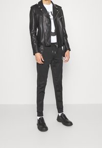 Svart skinnbikerjacka över en vit t-shirt med grafik, kombinerat med svarta snävna sweatpants och svarta snörskor.