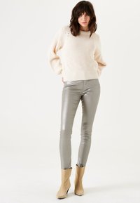 Crème gebreide trui met vlechttextuur, gecombineerd met metallic zilveren skinny broek en beige enkellaarsjes.