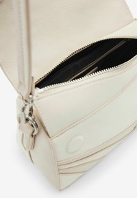 Crossbody-Tasche aus weichem beigen Leder mit Reißverschluss, schwarzem Stofffutter und dezenten Steppdetails. Mit abnehmbarem Riemen.