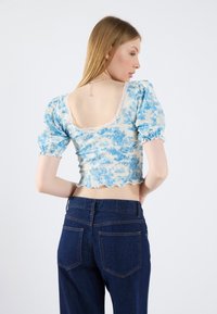 Blå blomsteret cropped top med pufærmer, blondekant og bølget kant. Kombineret med højtaljede mørkeblå denim jeans.