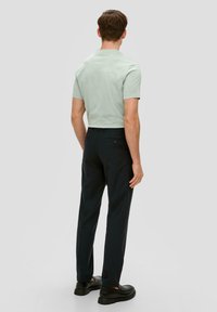 Hellgrünes kurzärmliges Hemd kombiniert mit dunkelgrauen Slim-Fit-Hosen, die eine Gesäßtasche haben, sowie schwarzen Schuhen. Einfaches, zeitgenössisches Design.