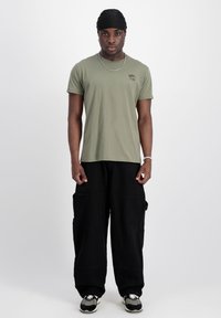 Olivgrön t-shirt med kort ärm och en liten grafik, kombinerad med lösa svarta cargo-byxor med sidofickor. Svarta sneakers med detaljer.