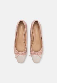 Ballerines roses pâles avec finition brillante, bout arrondi et capuchon de couleur crème contrastant. Présentent un petit nœud à l'avant.