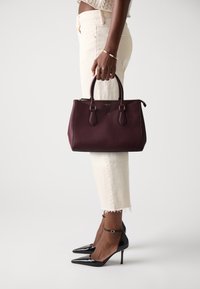 Burgundy handbag with smooth texture, structured shape, and dual top handles, paired with white cropped jeans and black pointed-toe heels.