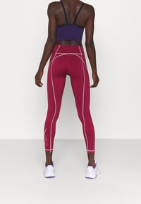 Leggings marmorizzati a bordeaux con cuciture grigio chiaro, vita alta e un design elegante. Abbinati a un reggiseno sportivo nero e viola e sneakers bianche.