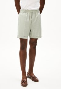 Lichtgroene linnen shorts met een elastische tailleband, koorddetails, zijzakken en een omgeslagen zoom. Bruine leren loafers completeren de look.