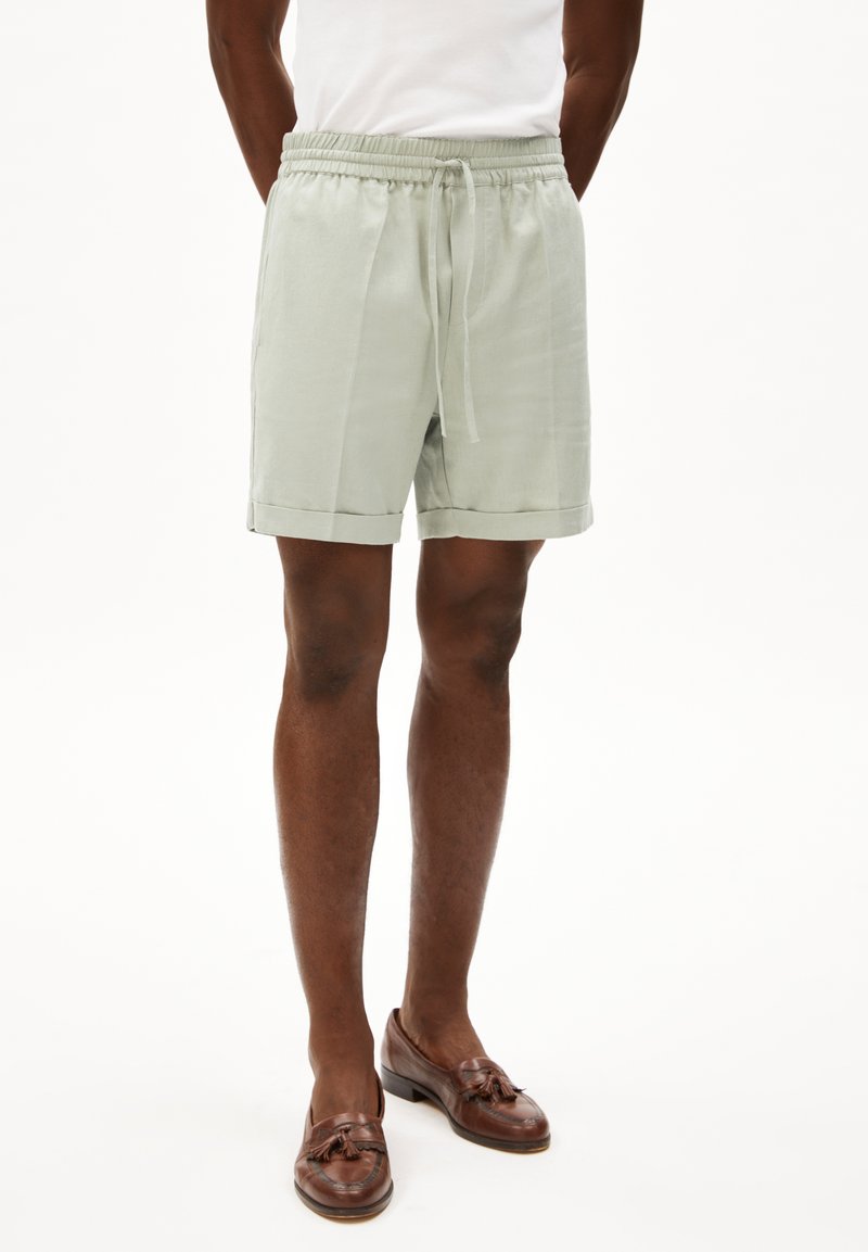 Lichtgroene linnen shorts met een elastische tailleband, koorddetails, zijzakken en een omgeslagen zoom. Bruine leren loafers completeren de look.