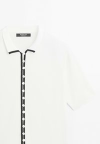 Wit poloshirt met korte mouwen en zwarte bies op de kraag en knopenlijst, met kleine witte knopen aan de voorkant.