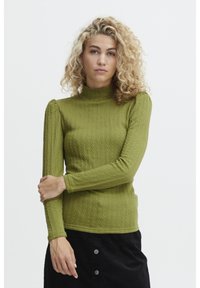 Maglione verde a coste con collo alto, maniche lunghe e un motivo testurizzato. Il modello sta incrociando le braccia davanti.
