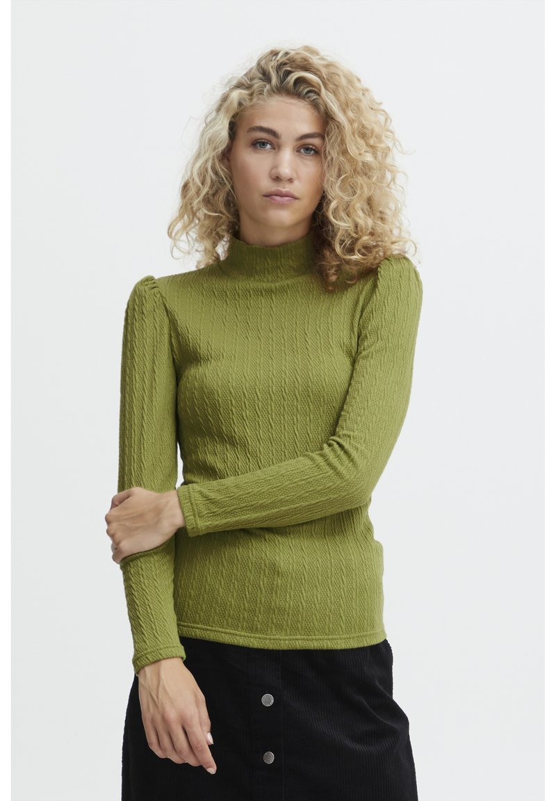Maglione verde a coste con collo alto, maniche lunghe e un motivo testurizzato. Il modello sta incrociando le braccia davanti.