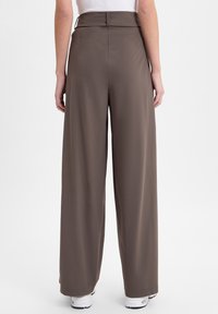 Weite Hose aus einem gedämpften braunen Stoff, mit hoher Taille, glatter Textur und bodenlanger Silhouette. Mit minimalen Nähten verarbeitet.