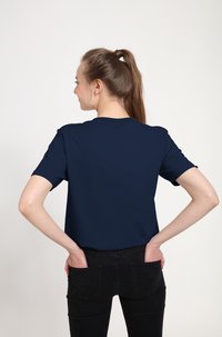Marineblaue Kurzarm-T-Shirt mit Rundhalsausschnitt, glatter Stoff, lockere Passform, getragen mit schwarzen Jeans, Hände in den Taschen, schlichte Rückansicht.