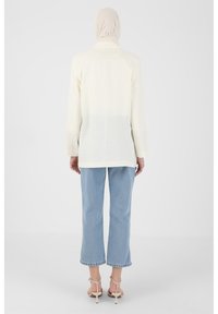 Light beige long blazer with a straight cut, featuring a soft texture and simple collar, paired with light blue cropped jeans.