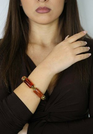 Braunes Armband mit rechteckigen rot-braunen Steinen und goldenen Akzenten. Das Design zeichnet sich durch glatte und glänzende Texturen sowie abgerundete Enden aus.