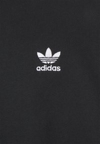 Felpa nera in cotone con un piccolo logo bianco Adidas e tre forme a foglia sopra il nome del marchio, su uno sfondo texturizzato.