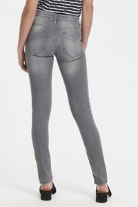 Jeans de denim gris ajustados con cintura alta, que cuentan con dos bolsillos en la parte posterior y una textura suave y lisa. Combinados con zapatos de tacón negros.