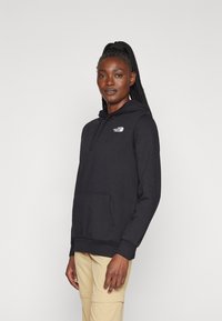 Black hooded sweatshirt made of cotton-blend material, featuring a front pocket and a small white logo on the chest. The cuffs are ribbed.