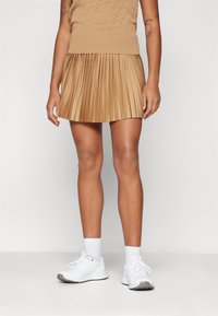 Tan plisserad mini kjol i lätt tyg, kombinerad med en beige stickad topp och vita sneakers, med ribbade detaljer vid fållen.