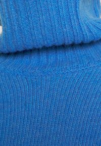 Pullover a collo alto di un blu brillante, realizzato a maglia con texture a coste visibili e dettagli di colletto piegato.