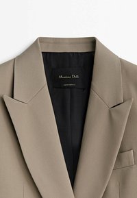 Beige, maßgeschneiderter Blazer mit scharfen Revers, einer Brusttasche und einem schwarzen Futter. Das Etikett trägt die Aufschrift "Massimo Dutti, hergestellt in Portugal."