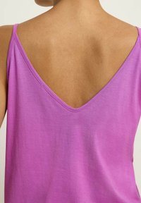 Lila ärmlös topp med en djup V-formad rygg, mjukt bomullsmaterial och slät textur med minimal sömnadsdetalj.