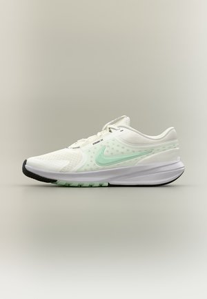 Zapatilla de correr Nike blanca con logo en verde claro y texto "Dynamic Fit" en el lateral, suela negra y blanca, mostrada sobre fondo neutro.