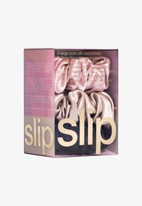 Three large silk scrunchies in blush, champagne, and black, packaged in a clear box with pink and gold branding and text.