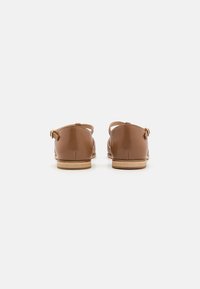 Bruine leren schoenen met een gladde afwerking, achteraanzicht toont een platte hak en gesp detail. Bevat beige accenten op de zool.