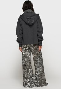Donkergrijze cropped hoodie met een gewatteerd patroon op de capuchon en het nummer "10" geborduurd. Gecombineerd met lichtgekleurde broek met een luipaardprint en wijde pijpen.