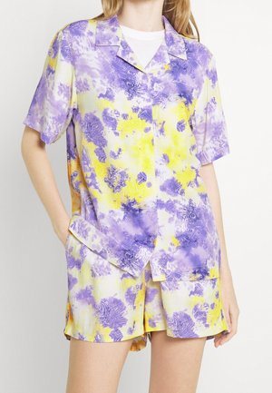 Conjunto de camisa de manga corta y pantalones cortos fabricado en un tejido ligero, con un patrón floral en amarillo y púrpura, con un corte relajado y cierre de botón.