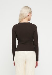 Maglia marrone a coste a maniche lunghe con design aderente e scollo rotondo, abbinata a pantaloni crema lavorati a trecce.