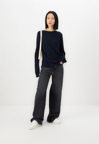 Marineblå genser med lange ermer, løs passform, kombinert med mørkegrå vide jeans og hvite sneakers. Minimalistisk kremfarget skulderveske.
