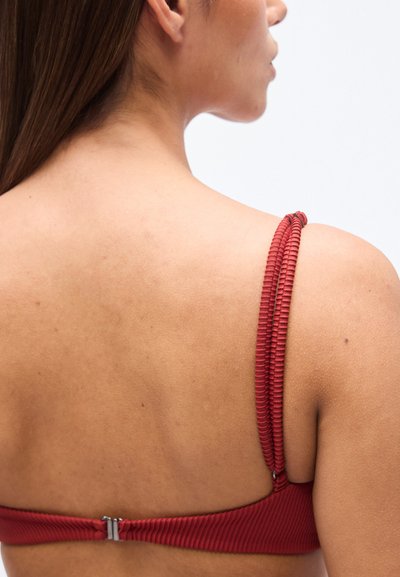 Κόκκινο μπικίνι τοπ με κυματοειδή υφή, λεπτές ρυθμιζόμενες τιράντες και κούμπωμα στο πίσω μέρος, που παρουσιάζει έναν κομψό, μινιμαλιστικό σχεδιασμό.