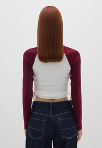 Langemouw t-shirt met een maroon raglan ontwerp en een witte stof, gecombineerd met hoge taille donkere spijkerbroek met zichtbare naden en zakken.