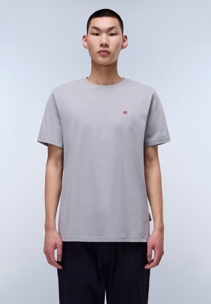 Camiseta de algodón gris con escote redondo, mangas cortas y pequeño detalle de bandera bordado en el pecho. Dobladillo recto con un corte relajado.