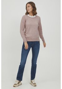 Maglione a maglia di un rosa chiaro con maniche a costine e colletto rifinito in pizzo, abbinato a jeans blu e sneakers beige.