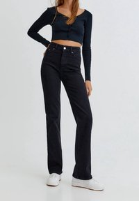 Jean noir taille haute avec une coupe droite, associé à un haut ajusté à manches longues foncé avec un design boutonné sur le devant. Des baskets blanches complètent le look.