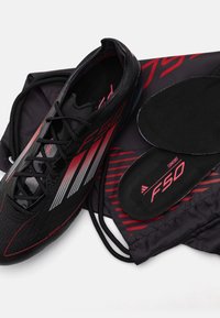 Scarpe da calcio nere con strisce rosse e grigie, caratterizzate da una tomaia texture e una soletta imbottita, accompagnate da una borsa con cordino coordinata.