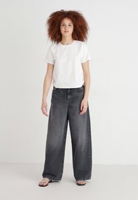 Hvid bomulds t-shirt kombineret med høj talje og bred ben mørkegrå denim jeans. Jeansene har en falmet vask og klassisk fem-lomme design.