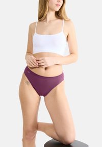 Paarse katoenen slips met elastische tailleband, gecombineerd met een witte bralette. Kenmerken zijn een gladde textuur en minimale naden.