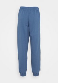 Blå träningsoverallsbyxor i mjukt tyg, med resårmidja, muddar vid anklarna och vita sidostråkar för extra detalj.