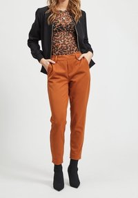 Chupa bomber negro sobre una blusa de estampado animal marrón, combinada con pantalones ajustados color óxido y botas de tacón texturizadas negras.