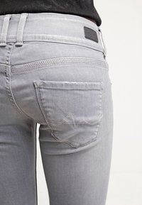 Jeans de mezclilla gris con un corte ajustado, costuras detalladas y un bolsillo trasero con un diseño de ola.