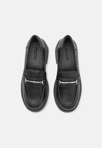 Sorte lærloafers med rund tå, med en sølvfarget detalj over fronten og teksturert innersåle. Merkevarelogo synlig inni.