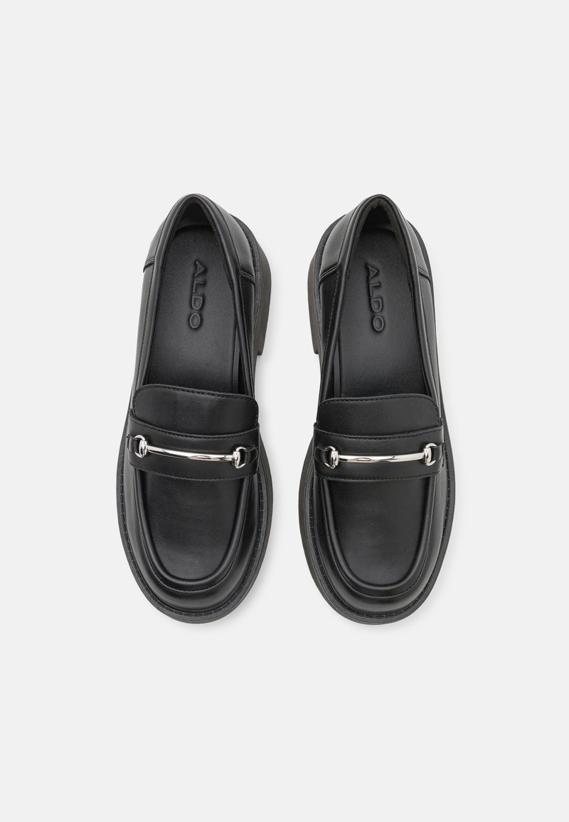 Mocassins en cuir noir avec un bout arrondi, arborant un accent argenté sur le devant et une semelle intérieure texturée. Logo de la marque visible à l'intérieur.
