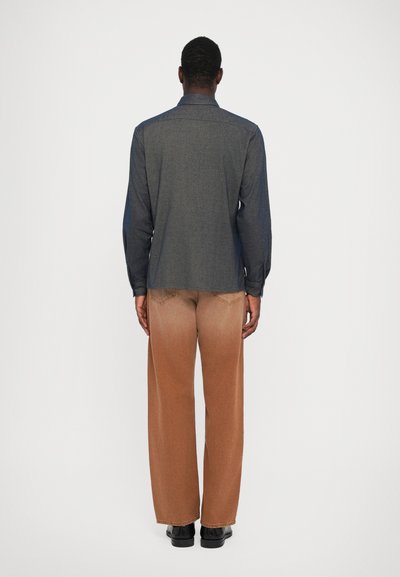 Cămașă din denim de un gri închis, prezentată din spate, cu mâneci lungi și guler standard. Pantaloni largi, de culoare maronie, cu un efect de gradient.