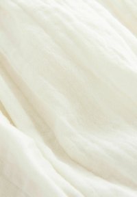 Tissu léger et texturé, de couleur blanche, avec une apparence douce et froissée. Le tissage est lâche, donnant une qualité légère et aérée.