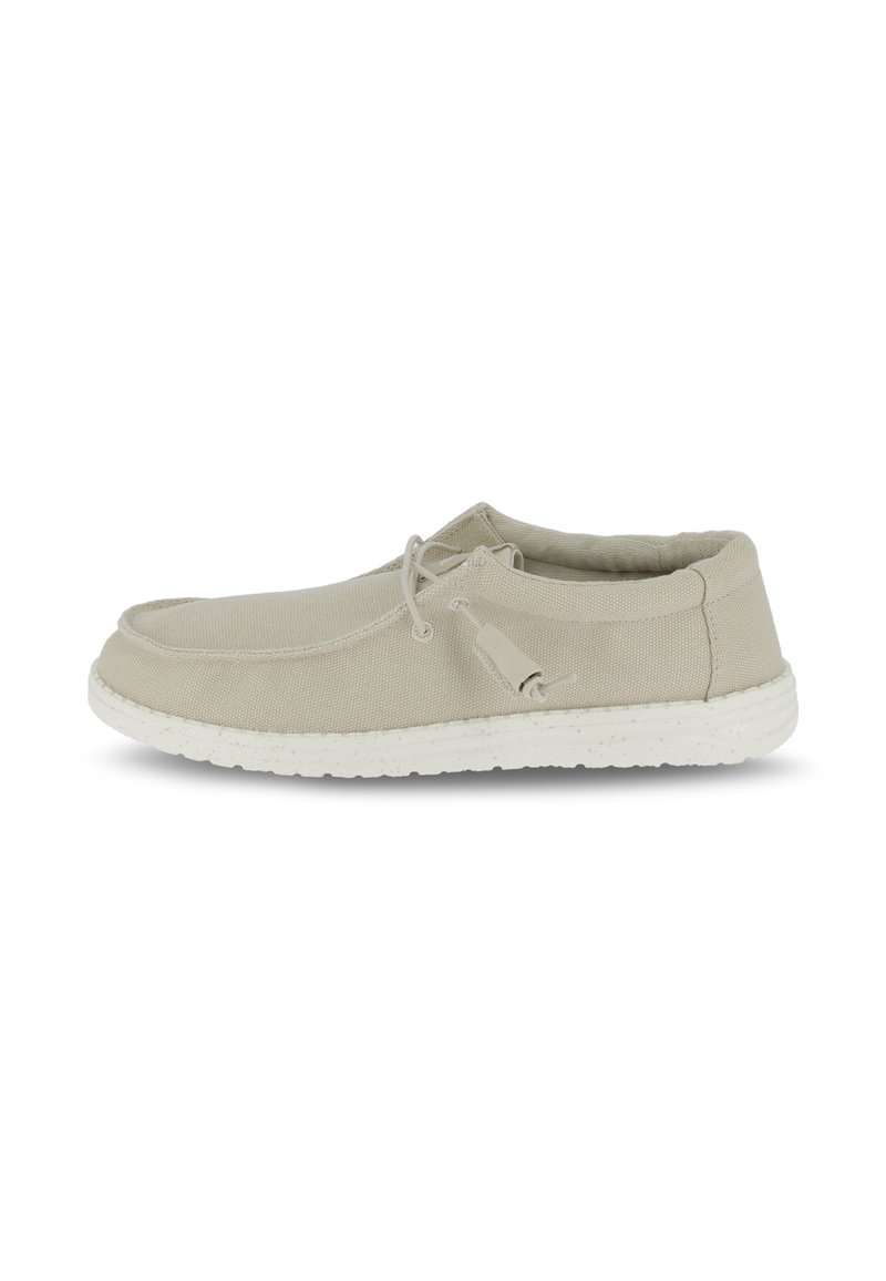 Scarpa in tela beige con forma arrotondata, suola in gomma bianca maculata e un design di lacci fissati sul lato.